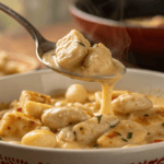 A close-up of a spoonful of creamy chicken and gnocchi with sauce dripping.