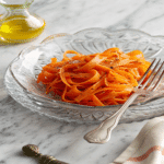 Ribbon Carrot Salad served in a glass bowl with olive oil and fork on marble table