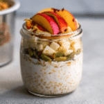 Apple Cinnamon Overnight Oats in a glass jar topped with apple slices, pumpkin seeds, and fresh fruit