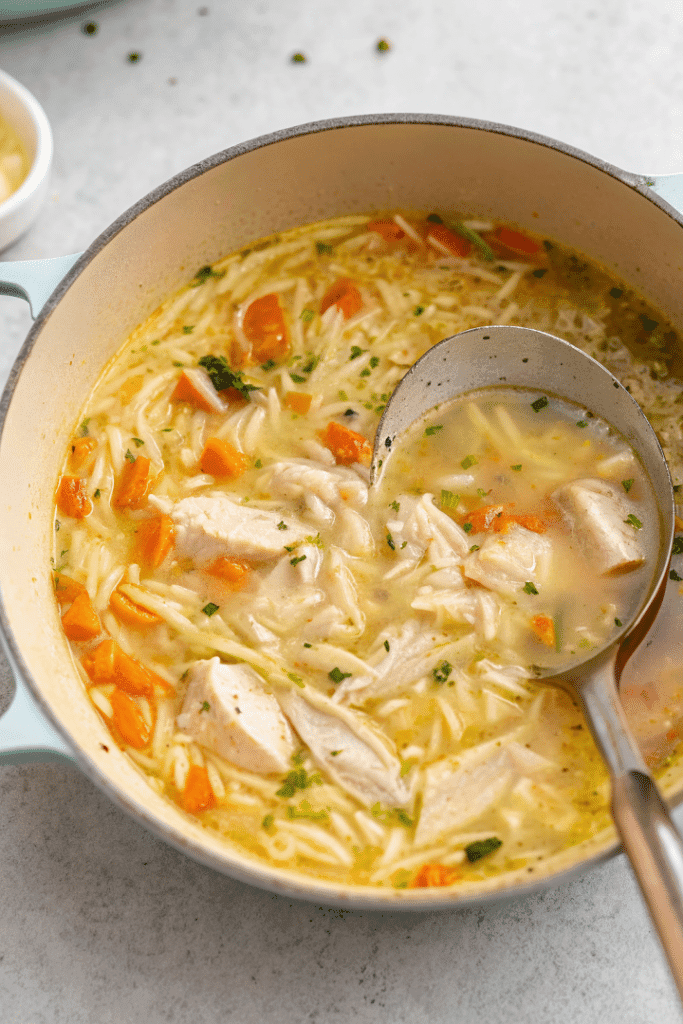 lemon chicken orzo soup simmering in a pot with ladle