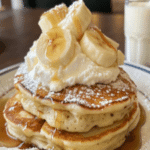 Sweet Coconut Cream Pancakes topped with bananas, whipped cream, and syrup
