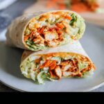Close-up of two halves of a Buffalo Chicken Wrap, showing shredded chicken, lettuce, carrots, and creamy sauce.
