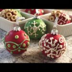 Close-up of red and green cake ball ornaments decorated with white and green icing, resembling Christmas ornaments.