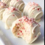 Close-up of a white chocolate-dipped Candy Cane Cake Pop, with a bite taken out, showing the cake and crushed candy cane interior.