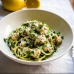 A close-up of a white bowl filled with Chicken Zoodle Alfredo, topped with chopped parsley and grated Parmesan cheese.