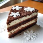A slice of Chocolate Snowflake Cake featuring layers of dark chocolate cake and white frosting, topped with chocolate crumbs and white snowflake decorations.