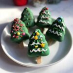 A plate of decorated green Christmas Tree Cake Pops with festive sprinkles and icing.