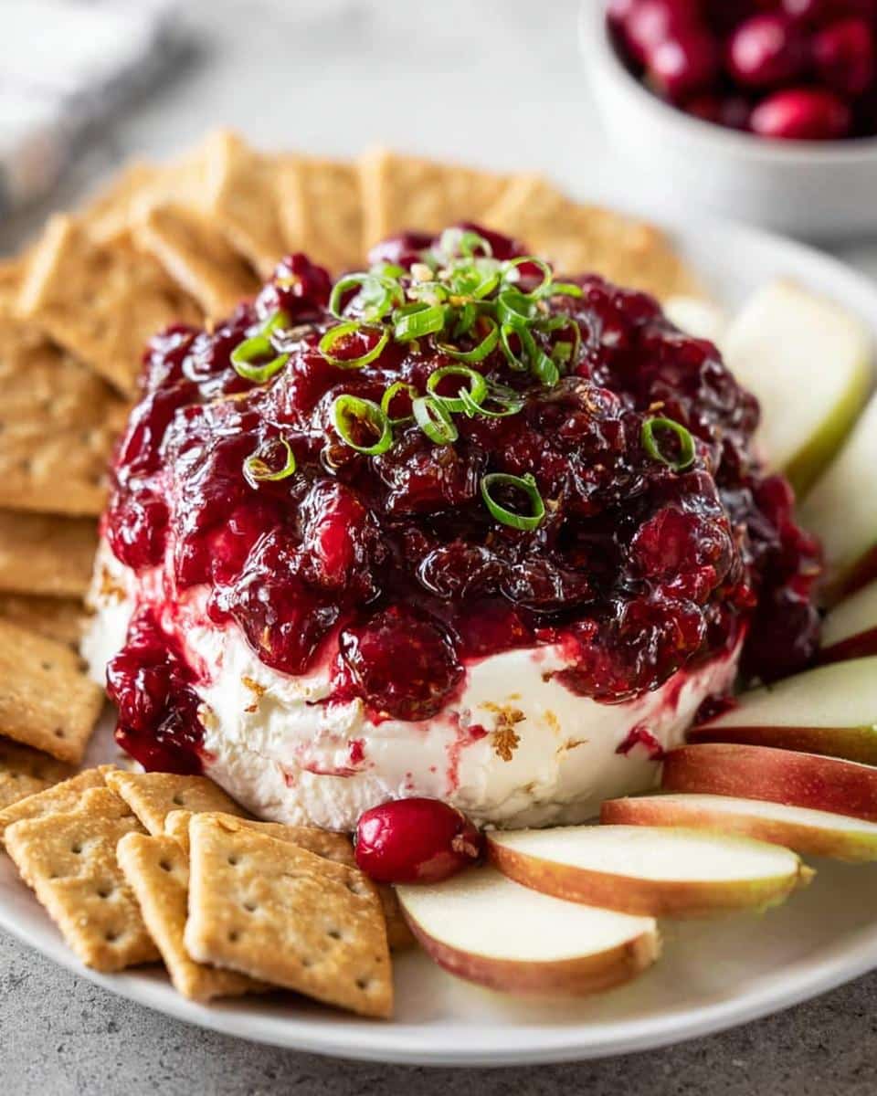 A festive Cranberry Cream Cheese Dip topped with cranberry sauce and green onions, served with crackers and apple slices.