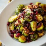 A close-up of delicious Cranberry Pecan Brussels Sprouts, glistening and topped with nuts and dried cranberries.