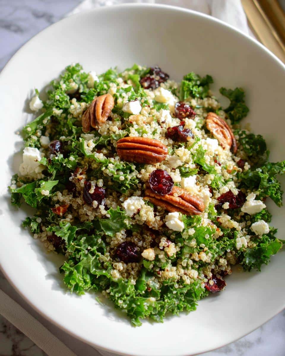 A vibrant Cranberry Pecan Quinoa Salad served in a white bowl, featuring kale, quinoa, dried cranberries, pecans, and feta cheese.