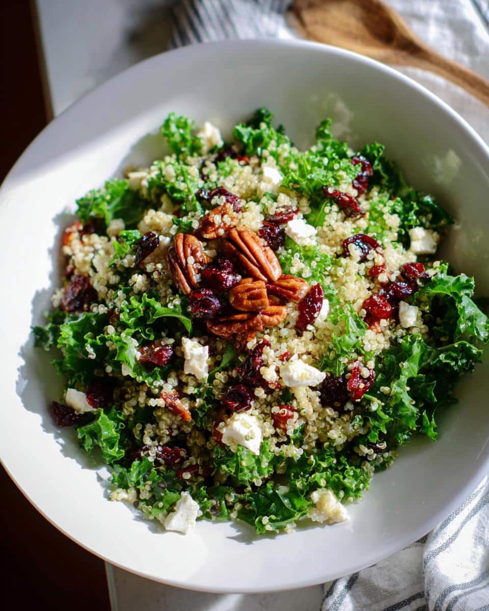 A vibrant Cranberry Pecan Quinoa Salad served in a white bowl, featuring kale, quinoa, dried cranberries, pecans, and feta cheese.
