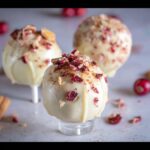 Close-up of three Cranberry White Chocolate Cake Pops, coated in white chocolate and topped with dried cranberries and crumbs.