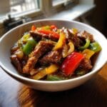 A steaming bowl of Crockpot Pepper Steak with Veggies, featuring tender beef strips and colorful bell peppers.