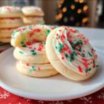 Close-up of Crumbl Copycat Sugar Cookies topped with white frosting and festive red and green sprinkles. One cookie is broken to show the soft interior.
