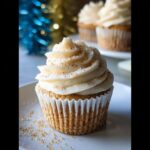 A festive eggnog cupcake topped with swirls of cream cheese frosting and sprinkled with edible glitter.