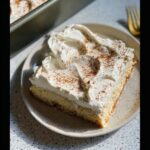A delicious slice of Eggnog Tres Leches Cake topped with whipped cream and dusted with cinnamon.