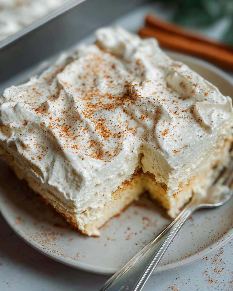 A slice of decadent Eggnog Tres Leches Cake topped with whipped cream and sprinkled with cinnamon.