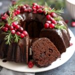 A slice of moist Gingerbread Chocolate Bundt Cake Wreath, glazed with chocolate and decorated with cranberries and rosemary.