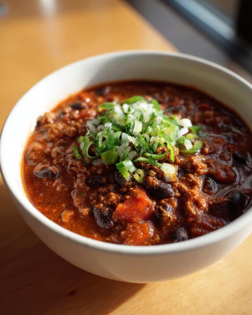 A bowl of healthy turkey chili in crockpot, topped with fresh chopped green onions and cilantro.