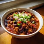 A close-up of a bowl filled with hearty Healthy Turkey Chili in Crockpot, topped with chopped onions, scallions, and peppers.