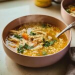 A steaming bowl of Italian Penicillin Soup, featuring shredded chicken, small pasta pearls, carrots, and fresh parsley.