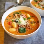 A close-up of a bowl of Italian Sausage and Spinach Gnocchi Soup, topped with shredded Parmesan cheese.