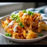 A fork lifts a cheesy bite from a Keto Buffalo Chicken Casserole topped with sour cream and green onions.