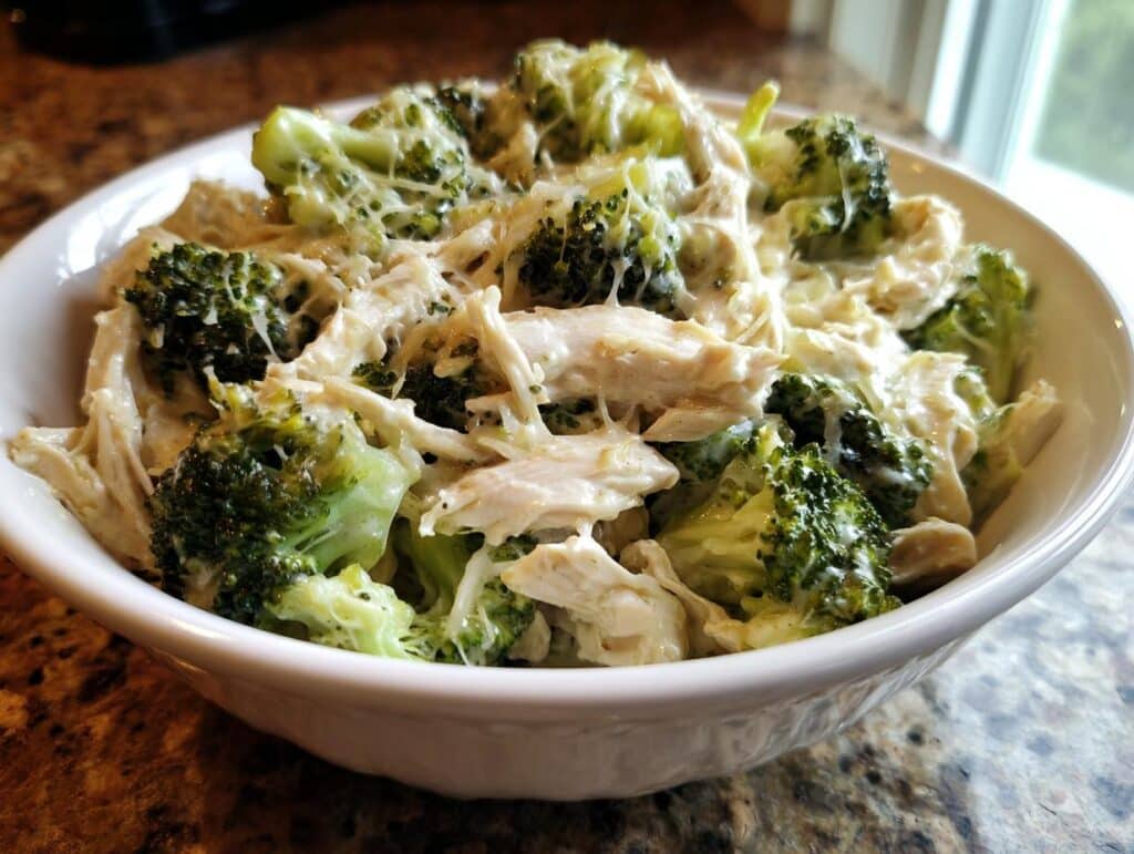 A white bowl filled with creamy Low-Carb Chicken Broccoli Alfredo Crockpot, featuring shredded chicken and vibrant broccoli florets in a rich sauce.