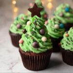 Close-up of a chocolate cupcake decorated with green frosting to resemble a Christmas tree, topped with a chocolate star and edible ornaments.