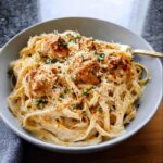 A close-up of a bowl of One Pot Cajun Chicken Alfredo Pasta, featuring creamy fettuccine, seasoned chicken pieces, and a sprinkle of parsley and paprika.
