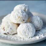 A close-up of a pile of Pecan Snowball Cookies dusted generously with powdered sugar.