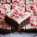 A close-up of a Peppermint Bark Brownie Bite, showcasing the rich chocolate brownie base topped with white chocolate and crushed candy canes.