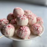 A pile of festive Peppermint Bark Cake Pops coated in white chocolate with red drizzles and crushed candy cane.