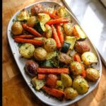 A platter of colorful roasted potatoes, carrots, and zucchini, seasoned with herbs.
