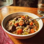 A steaming bowl of Slow Cooker Beef Barley Soup with tender beef chunks, carrots, barley, and herbs.