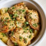 Close-up of tender Slow Cooker Garlic Parmesan Chicken thighs nestled with potatoes, garnished with fresh parsley and grated Parmesan cheese.