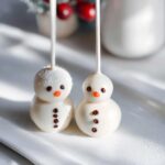 Two cute Snowman Cake Pops decorated with white chocolate, orange noses, and chocolate chip buttons.