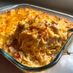A fork lifting a cheesy bite of Spicy Southern Chicken Spaghetti Casserole from a baking dish.