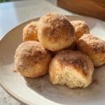 Close-up of several 2-Ingredient Baked Banana Donut Holes coated in cinnamon sugar on a light plate.