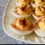 Close-up of creamy Deviled Eggs with Paprika sprinkled over the filling, served on a light platter.
