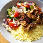 A close-up of Air Fryer BBQ Chicken Bowls featuring seasoned chicken pieces over fluffy couscous with a fresh tomato, cucumber, red onion, and feta salad.