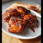 Four perfectly cooked Air Fryer BBQ Chicken Thighs glazed with sauce on a white plate.
