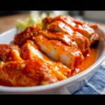 Close-up of sliced Air Fryer Buffalo Chicken, coated in spicy orange sauce, served in a white dish.