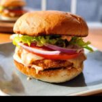 A close-up of a delicious Air Fryer Chicken Burger with lettuce, tomato, onion, and sauce on a bun.