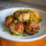 A plate of four golden-brown Air Fryer Chicken Meatballs, garnished with chopped green onions, served with a side of shredded carrots.