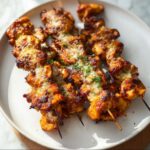 Close-up of several juicy air fryer chicken skewers topped with melted cheese and parsley on a white plate.