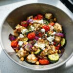 A bowl of Air Fryer Greek Chicken with Veggies, featuring grilled chicken, cherry tomatoes, zucchini, red onion, chickpeas, and feta cheese.