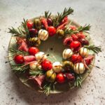 Appetizer skewers arranged in a circle like an Antipasto Christmas Wreath, featuring mozzarella balls, cherry tomatoes, olives, and salami.