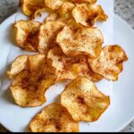 Close-up of crispy, baked Apple Cinnamon “Chips” dusted heavily with cinnamon spice on a white plate.