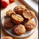 A stack of freshly baked Apple Cinnamon Protein Muffin Bites, dusted heavily with cinnamon sugar, served on a white plate.